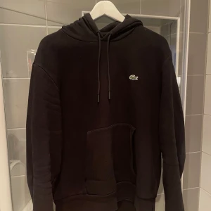 Svart Lacoste Hoodie - Svart hoodie från Lacoste i jättefint skick. Super skön och stilren hoodie som passar till allt. Tröjan är i storlek Large. Kan gå ner i pris vid snabb och smidig affär. Hör av er vid frågor!