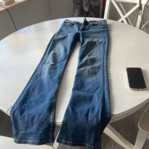 Blå bootcut jeans från Zara, stl 36 - Snygga blå jeans från Zara i klassisk bootcut-modell. Jeansen har fem fickor, normal passform och är tillverkade i jeansmaterial. Färgen är mellanblå med lätt slitning och råa kanter nertill för en cool vibe.