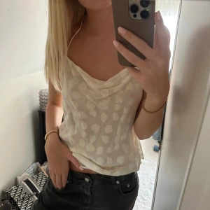 Vit mönstrad linnetopp från H&M - Supersöt vit linnetopp från H&M i storlek XS. Toppen har tunna axelband som knyts i nacken och öppen rygg. Tyg med diskret mönster och lätt glansig känsla, perfekt för varma dagar. Snygg drapering framtill och luftig passform. Aldrig använd 