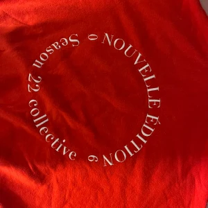 Röd hoodie från Boohoo med tryck - Cool röd hoodie från Boohoo med vit text i cirkel på ryggen där det står 'Nouvelle Édition Season 22 collective'. Tröjan har huva med snörning och breda muddar. Perfekt för dig som vill sticka ut med en färgstark och trendig look.