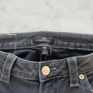 Svarta low waist bootcut jeans från True Religion - Snygga svarta jeans från True Religion med bootcut passform. Jeansen har klassiska kontrastsömmar, silverfärgade knappar och detaljerade bakfickor med lock. Tillverkade i mjukt denimtyg som ger en skön känsla och cool look. Jag har bara använt dessa ett fåral gånger och original priset är 1100 kr. Jag säljer dessa för nu för att de är för korta för mig som är 179 cm lång🥲