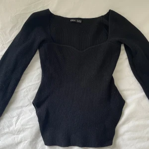 Svart ribbad topp från SHEIN - Svart långärmad topp från SHEIN med ribbad struktur och markerad sweetheart-urringning. Figurnära passform som framhäver midjan och ger en snygg siluett. Perfekt att styla med jeans eller kjol för en trendig look.