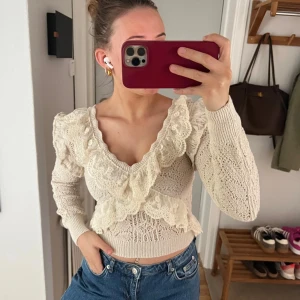 Krämvit spetsblus från Zara - Säljer en romantisk krämvit spetsblus från Zara med volangdetaljer och v-ringning. Blusen är croppad och har långa ärmar samt ett vackert mönster i spets. Perfekt för dig som gillar feminina detaljer och unik stil.