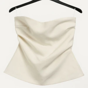 Vit axelbandslös tubtopp från Zara - Säljer en stilren vit tubtopp från Zara i axelbandslös modell. Toppen har en lätt draperad framsida och är sydd i ett slätt tyg som ger en elegant känsla. Perfekt för dig som gillar minimalistisk och trendig stil.