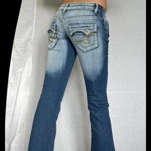 Blå bootcut jeans från B&J Jeans - OANVÄNDA Bootcut jeans i blå denim från B&J Jeans med slitna detaljer och patchar på knäna. Bakfickorna har lock och dekorativa kedjor i gult.💗