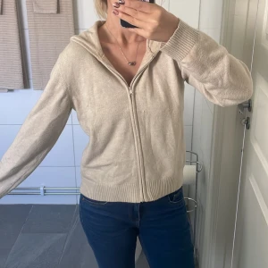 Beige hoodie med dragkedja - Mysig beige hoodie med dragkedja framtill och huva. Tröjan har ribbade muddar vid ärmslut och nederkant, samt en avslappnad passform. Perfekt för lager-på-lager och chill dagar.