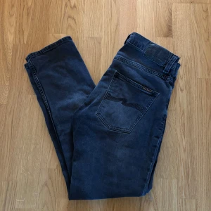 Nudie Jeans Grim Tim 30/30 - Snygga gråa slimfit jeans ifrån märket Nudie Jeans perfekta till hösten. Modellen på jeansen heter Grim Tim Färgen heter Dark Cove Storleken är 30/30 och passar dig som är mellan 175-180 cm