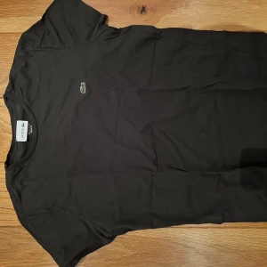 Grön t-shirt från Lacoste - Grön t-shirt från Lacoste med klassisk krokodillogga broderad på bröstet. T-shirten har rund halsringning och är tillverkad i mjuk bomull. Enkel och stilren modell som passar perfekt till jeans eller shorts.