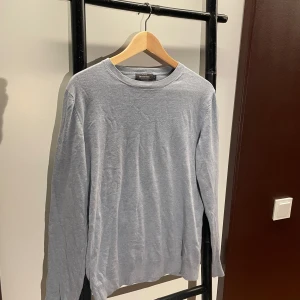 Ljusblå bomullströja från Dressmann - En stilren ljusblå långärmad tröja från Dressmann i mjuk Supima-bomull. Tröjan har rund halsringning och klassisk passform, perfekt för en clean och enkel look. Passar dig som gillar basic och bekvämt. 