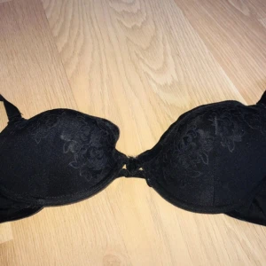 Vintage bh  - Snygg svart korsett-topp med vadderade kupor och blommiga sammetsdetaljer. Axelbanden är justerbara och tyget är mjukt med en elegant känsla. Perfekt för att ge outfiten en extra edge och passar till många olika stilar. 