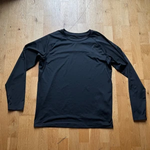 Svart långärmad sporttröja Best Fashion - Svart långärmad sporttröja från Best Fashion i storlek L. Tillverkad i mjuk och stretchig polyester med elastan, perfekt för träning. Tröjan har rund hals och en clean, enkel design utan mönster eller detaljer. Sitter bekvämt och är lätt att röra sig i.