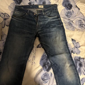 Blå jeansbyxor från Tiger of Sweden - Snygga blå jeansbyxor från Tiger of Sweden med klassisk femficksdesign och läderpatch bak i midjan. Jeansen har en rak passform och subtila slitningar framtill för en cool look. Perfekta för dig som gillar stilrena och tidlösa jeans. Najs wash.