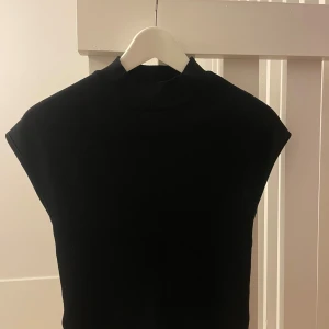 Svart stickad polotopp från mango - Säljer en svart stickad polotopp från MNG i storlek XS. Toppen har hög krage och är ärmlös med en clean, rak passform. Perfekt att styla med jeans eller kjol för en snygg look. Materialet är mjukt och stretchigt för extra komfort. Nypris 400