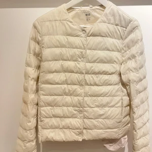 Vit pufferjacka från Uniqlo!! - Säljer en stilren ljusbeige pufferjacka från Uniqlo med PUFFERTECH. Jackan är lätt, har rund halsringning och knäpps med tryckknappar framtill. Perfekt för lager-på-lager och enkel att matcha med allt.