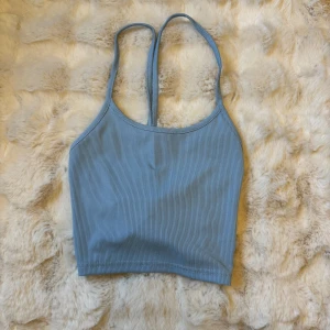 Blå ribbad linnetopp med snörning - Säljer en ljusblå ribbad linnetopp med smala axelband och snygg snörningsdetalj i ryggen. Toppen är croppad och har en enkel, stilren design som passar perfekt till jeans eller kjol. Materialet är mjukt och stretchigt för en bekväm passform.