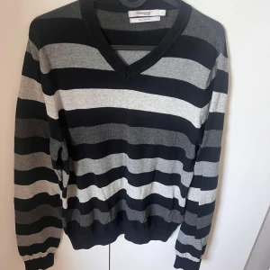 Randig v-ringad tröja Dressmann S - Snygg v-ringad tröja från Dressmann i storlek S, med breda svarta och gråa ränder. Tillverkad i mjuk pima bomull som känns skön mot huden. Långärmad modell med ribbade muddar vid ärmslut och nederkant. Perfekt för dig som gillar klassisk stil med en modern twist.