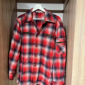 Röd rutig overshirt  - Röd och blå rutig overshirt tillverkad i Italien. (Även köpt i Italien) Skjortan har långa ärmar, knappar framtill och coola dragkedjefickor på bröstet och ena ärmen. Pris satt ex frakt