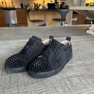 Christian Louboutin svarta sneakers med nitar - Svarta sneakers från Christian Louboutin i mocka med svarta nitar på tån och klassisk röd sula. Äkta, köpta i london för 8200kr för 2 år sen. Kommer inte till användning.  Pris kan diskuteras, vill bara bli av med dem
