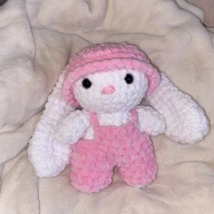 Hand virkad kanin - Supersöt rosa virkade byxdress till mjukisdjur, med fluffigt garn och hängslen. Byxdressen är handgjord och passar perfekt till gosedjur eller som dekoration. Mjuk och gosig känsla med tydlig struktur i materialet.