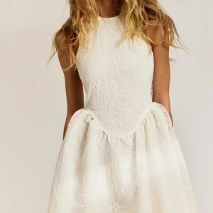 Vit spetsklänning med rosett - Superfin vit kortklänning i spets med blommigt mönster och stor rosett i ryggen. Klänningen är ärmlös, har en markerad midja och en voluminös kjol. Säljer denna klänning då den aldrig kommit till användning och har prislappen på. Köpt för 700kr säljer nu för 450kr pris kan diskuteras💗