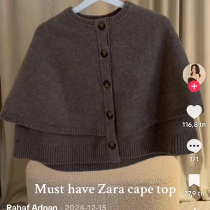 Grå stickad cape-topp från Zara - Superfin grå cape-topp från Zara i stickat material. Modellen är croppad med bred ribbad kant och stora knappar framtill. Perfekt för lager-på-lager och ger en chill men ändå snygg vibe.