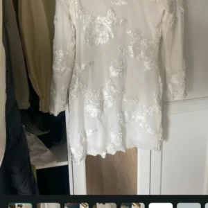 Vit blommig kortklänning från BYIC - Superfin vit kortklänning från BYIC med broderade blommor över hela klänningen. Klänningen har långa ärmar och en lätt transparent känsla med vackra detaljer. Perfekt för dig som vill sticka ut med en romantisk och fräsch look. Använd ändast en gång. Kostade 900 