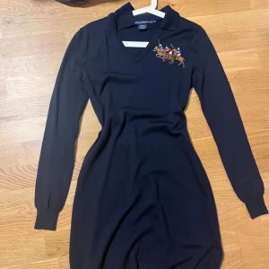 Mörkblå stickad klänning Ralph Lauren - Mörkblå stickad klänning från Ralph Lauren Sport med broderat polospel-motiv på bröstet. Klänningen har v-ringning, krage och långa ärmar. Tillverkad i 100% merinoull och har en klassisk, sportig look som sticker ut. Står L men passar mer S!!