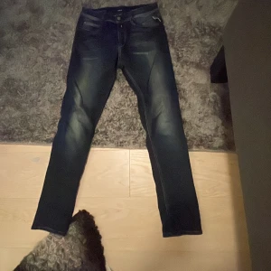 Replay Hyperflex mörkblå jeans - Säljer ett par Replay Hyperflex jeans i mörkblå tvätt med snygga slitningar. Jeansen har klassisk femficksdesign, smal passform och stretchigt material som gör dem riktigt bekväma. Perfekta för dig som gillar stilrena och moderna jeans.