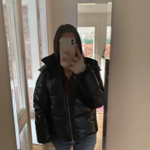 Svart glansig pufferjacka med huva - Svart glansig pufferjacka från nelly. Super fin i nästan nytt skick med inga märken eller skador. Ny pris är 799. 