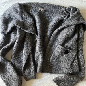 Grå stickad kofta  - Mysig grå stickad kofta från Iindex med lång ärm och en stor ficka framtill med knapp. Perfekt för lager-på-lager och chill dagar. Koftan har en lös passform och är superenkel att matcha med allt.