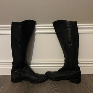 Svarta boots från Freeflex stl 38 - Säljer ett par klassiska svarta boots från Freeflex i storlek 38. Stövlarna är tillverkade i skinn med dragkedja på insidan och har låg klack samt rund tå. Perfekta för dig som gillar stilrena och tidlösa boots.