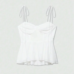 Vit korsett-topp med knytband - Supersöt vit korsett-topp med tunna axelband som knyts på axlarna. Toppen har en figurnära passform med markerade kupor och lätt utsvängd nederdel. Perfekt för varma dagar och ger en romantisk vibe till din outfit.