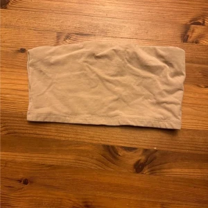 Beige bandeau tubtopp från 157 - Säljer en enkel och stilren beige bandeau tubtopp från 157 i storlek XS/S. Toppen är ärmlös och axelbandslös, perfekt för varma dagar eller som lager under skjortor. Mjuk och stretchig bomullskvalitet för skön passform.