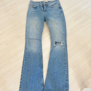 Blå bootcut jeans med slitning - Snygga blå jeans med bootcut passform och slitning på ena knät. Klassisk femficksmodell med dragkedja och knapp. Perfekta för dig som gillar en avslappnad och trendig look.