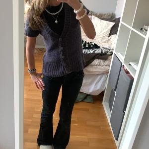 Söt stickad kofta  - Kortärmad stickad kofta i mörklila med djup v-ringning och bred ribbad kant nertill. Fem knappar framtill i matchande färg. Perfekt att slänga över en t-shirt eller linne för en chill och trendig look. Den är mörklila/brun. Osäker på märket . Storlek S men passar mig som har XS.