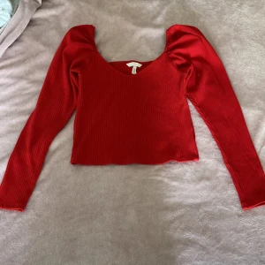 Röd ribbad långärmad topp H&M - Snygg röd ribbad topp från H&M med lång ärm och croppad passform. Toppen har en djup rundad ringning och lätt puffade axlar för en trendig look. Perfekt att styla med jeans eller kjol för en cool vibe.