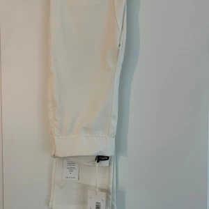 Byxor  - Krämvita byxor med slits från Bianca Ingrosso x Nelly kollektionen, stl 34 aldrig använda. Dragkedja på sidan.