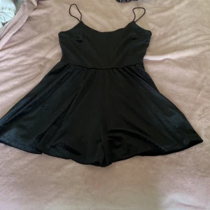 Svart kort klänning från H&M Divided - Svart kort klänning från H&M Divided med tunna axelband och lätt glansigt tyg. Enkel och stilren design med utställd kjol och smickrande passform. Perfekt för dig som gillar minimalistisk stil och vill ha något bekvämt men snyggt. Det finns också inbyggda short i klänningen 😁