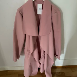 Lång kappa rosa - Snygg rosa kappa från Zara. Jackan har långa ärmar och ett elegant fall framtill. Perfekt för dig som vill ha en stilren och trendig look under kyligare dagar. Storlek S/M