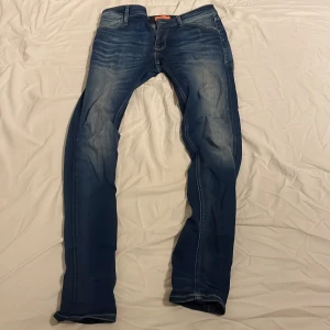 Blå jeansbyxor från Jack n Jones  - Snygga blå jeansbyxor med klassisk tvätt och lätt slitning på låren. Modellen är rak och passar dig som gillar en tidlös look. Jeansen har fem fickor och stängs med dragkedja och knapp. Perfekta för dig som vill ha ett par stilrena jeans i garderoben.