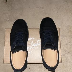 Svarta sneakers från Christian Louboutin - Snygga mörkblåa sneakers från Christian Louboutin i mocka med klassisk röd sula. Skorna har rund tå, svarta skosnören och diskreta metalldetaljer vid snörningen. Perfekta för dig som vill ha en stilren men ändå lyxig look. Skick: 7/10 lite använda men enda bra skick. Tar gärna byten mot philipmodell och valentinos flycrews i storlek 42.