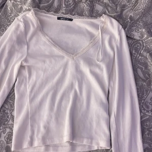 Vit ribbad långärmad topp Gina Tricot - Säljer en vit långärmad topp från Gina Tricot i ribbat material. Toppen har v-ringning med spetskant som ger en söt touch. Perfekt att styla med jeans eller kjol för en enkel men snygg look.