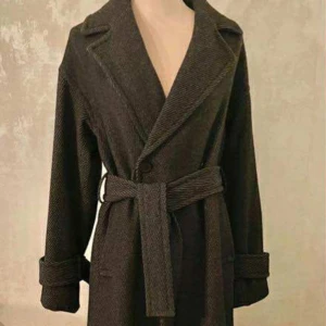 MQ - Monica coat - Mörkgrå omlottkappa med bälte - Snygg mörkgrå kappa i omlottmodell från Stockh lm studio - med bälte i midjan och breda slag. Jackan har långa ärmar med uppvikta muddar och är tillverkad i ett ulligt material med diskret randigt mönster. Perfekt för dig som gillar en stilren och trendig look.Som nyskick - använd endast ett fåtal gånger. Fodrad insida.   Material: 50% ull 50% polyester Foder: 55% polyester 45% viskos Sleeve. Längd bak: 126 cm i strl XS. Passform: Avslappnad. Nypris: 1999kr