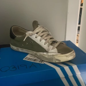 Philippe Model sneakers i olivgrönt - Snygga Philippe Model sneakers i olivgrönt och vitt med svarta detaljer på hälen. Skorna har klassisk snörning, vit sula och rund tå. Materialmix av skinn och syntet ger en exklusiv känsla. Perfekta för dig som gillar streetstyle med en twist. Storlek är 40 och man får med två kort också.