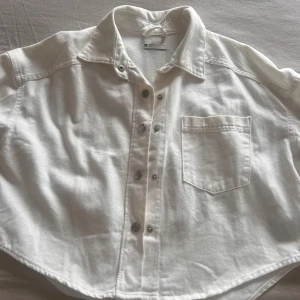 Vit overshirt från g perfect jeans - Säljer en vit overshirt från g perfect jeans i jeansmaterial. Skjortan är 100% bomull, har klassisk krage, tryckknappar och en bröstficka. Modellen är lite boxig och passar perfekt till lager-på-lager. Långärmad och enkel att styla till olika looks.
