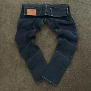 Mörkblå Replay Anbass jeans - Snygga mörkblå Replay Anbass jeans med klassisk femficksdesign, kontrastsömmar och detaljerad dragkedja på myntfickan. Jeansen har en rak passform och är tillverkade i slitstarkt denim. Perfekta för dig som gillar stilrena och tidlösa jeans.