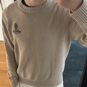 Beige stickad tröja från Morris  - Snygg beige stickad tröja från Morris med broderad logga på bröstet. Rund hals och ribbade muddar vid ärmslut och nederkant. Perfekt för dig som gillar klassisk stil med en modern touch. Priset kan såklart diskuteras 
