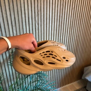 Yeezy 700 - Säljer ett par beige adidas Yeezy Foam Runner med futuristisk design och massor av hål för extra ventilation. Skorna är gjorda i syntetmaterial och har en chunky, vågig sula. Perfekta för dig som vill sticka ut med en unik och bekväm look. Saknar box.