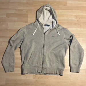 Grå hoodie från Polo Ralph Lauren - Det grå hoodie från Polo Ralphlauren i storlek L. Tröjan är i nyskick men en liten fläck på högerarm. Priset kan diskuteras 