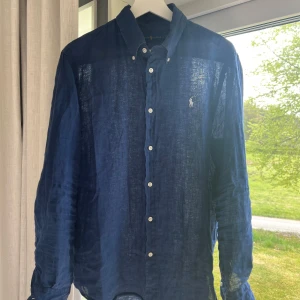 Ralph Lauren Linneskjorta - Säljer en mörkblå långärmad skjorta i linne från Ralph Lauren. Skjortan har klassisk krage, knappar framtill och den ikoniska broderade loggan på bröstet. Perfekt för en stilren och avslappnad look. Sitter som en Large, hör av er om ni har några frågor!